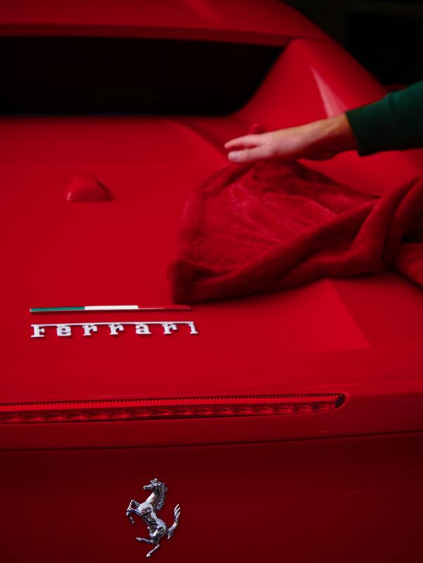 A hand wiping the rear of a red Ferrari with a microfiber towel