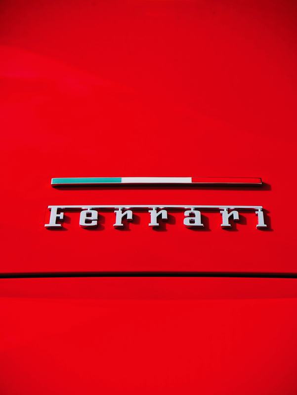 Close-up of a chrome Ferrari script badge on deep red paint