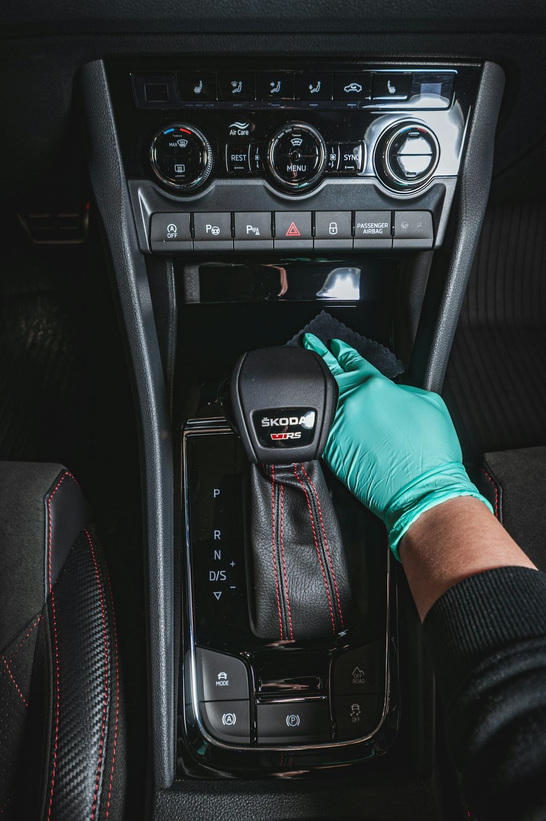 A gloved hand wiping down a car's gear shifter and center console