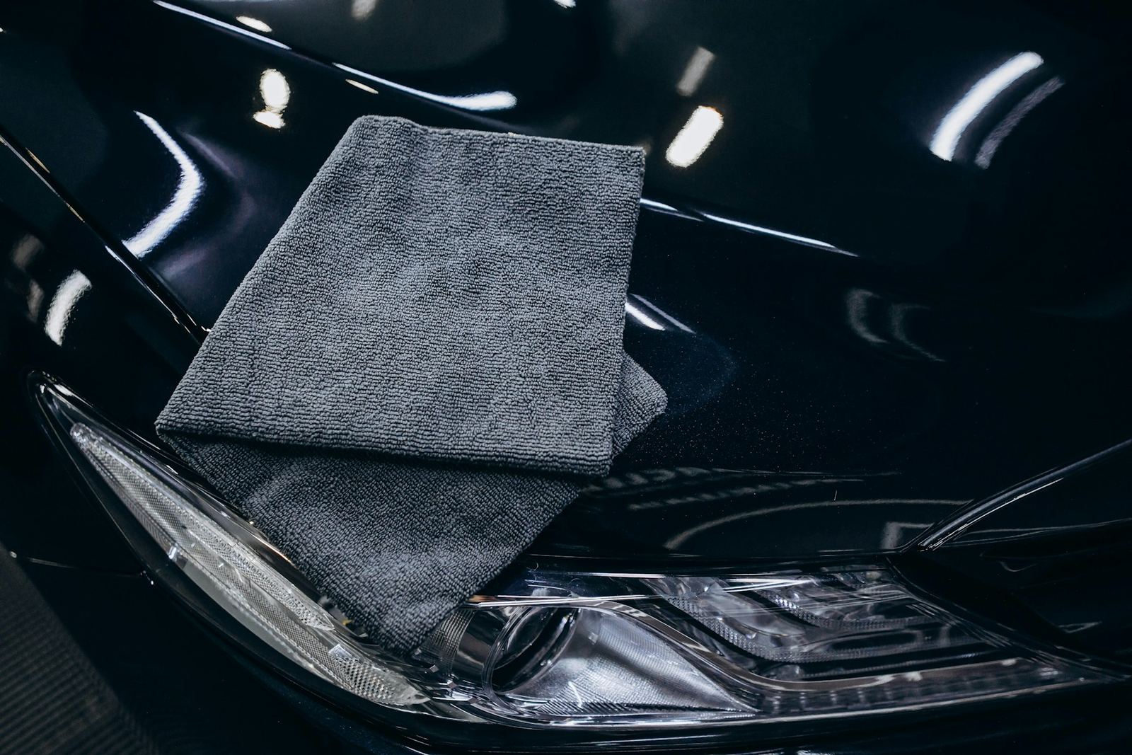 A folded grey microfiber towel resting on a glossy black car hood
