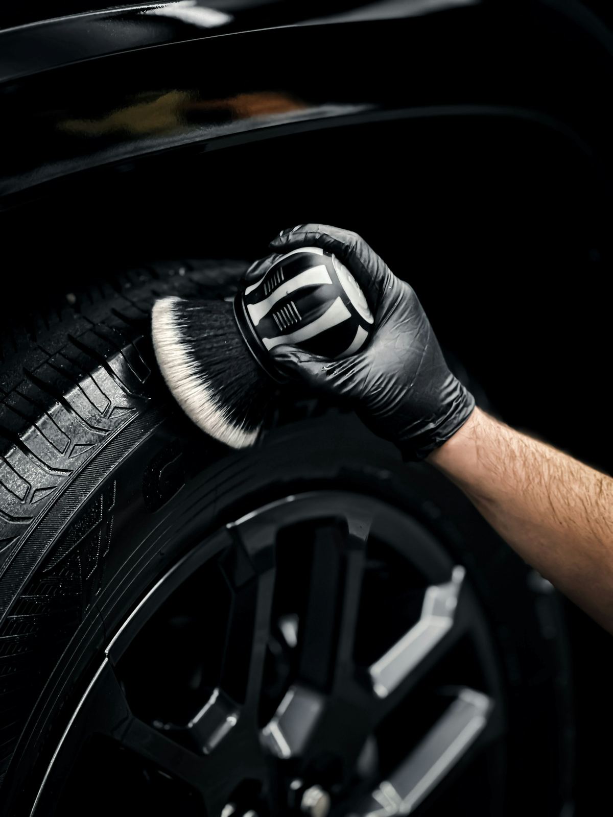 A gloved hand scrubbing a black tire with a detailing brush
